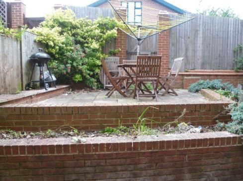 Trädgården (om man ens kan kalla den så) är liten. Minimal. Bilden visar i princip hela. Lägg märke till det fiffiga utnyttjandet av parasoll-hålet i bordet för torkvindan. Utanför staketet har vi vår parkeringsplats och sen ser man polisstationen sticka upp.